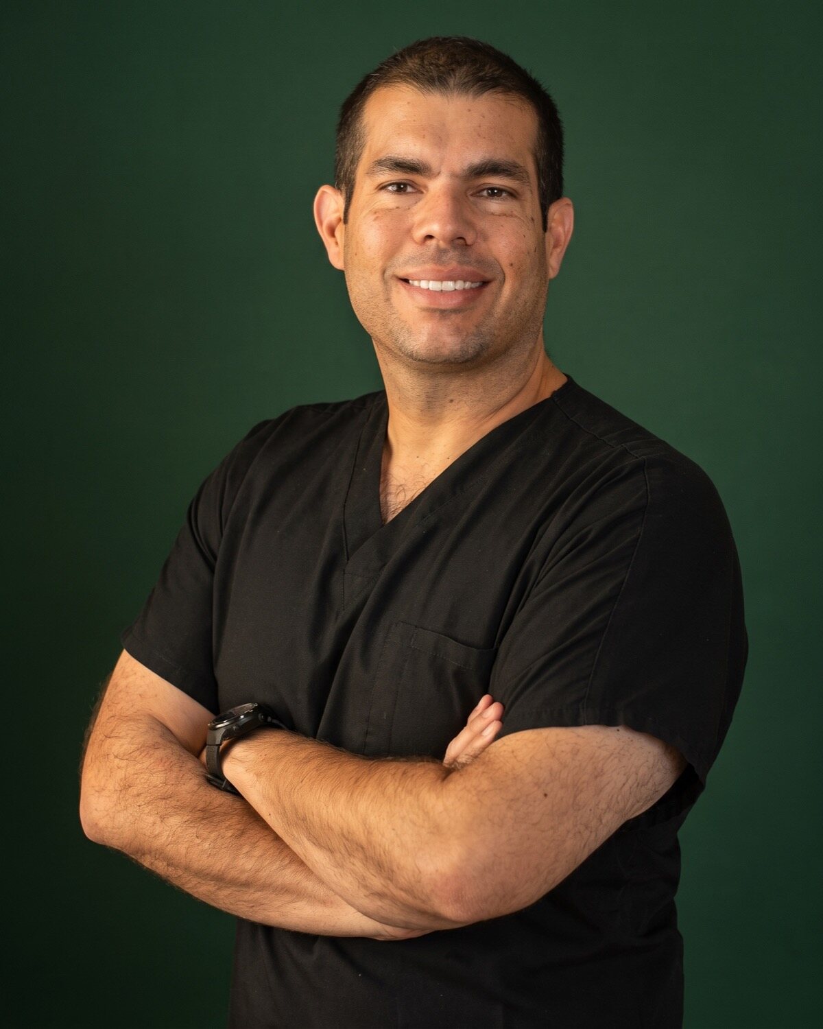 Studio portrait of Carlos Aguilar León, DDS, Harvard-trained implantologist and prosthodontist, arms crossed in black scrubs
